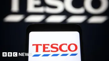 O logotipo da Tesco � exibido em um smartphone, contra um fundo preto exibindo uma vers�o maior e desfocada do logotipo do supermercado.