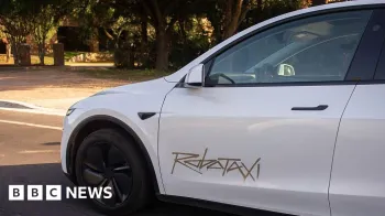Getty Images Close-up of a white Tesla robotaxi with no driver that has the word robotaxi painted on it in gold on the door
