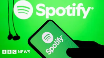 A silhueta de uma m�o segura um telefone com o logotipo verde e branco do Spotify. No fundo, pendem alguns fones de ouvido com fios pretos.