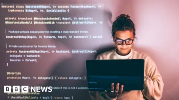 Uma mulher usando �culos com o cabelo preso parece sorrir segurando um laptop na m�o direita enquanto digita com a esquerda. O c�digo de programa��o aparece no lado esquerdo atr�s dela como um pano de fundo.