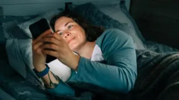 Getty Images Mulher sorrindo usando smartphone na cama � noite
