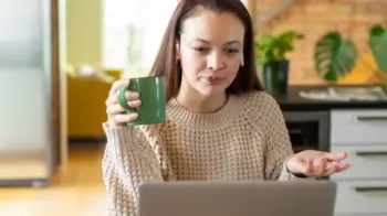 Getty Images A young woman holds a green mug and looks exasperated at an open laptop
