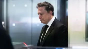 Getty Images Musk, wearing a black suit, white shirt and black tie, looks down toward the floor while waiting to pass through security at a courthouse in California.