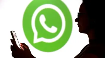Reuters Uma adolescente posa para uma foto segurando um smartphone na frente do logotipo do WhatsApp