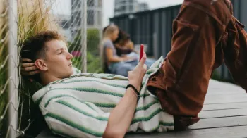 Um jovem deitado no ch�o usando um smartphone. A imagem ilustra como usamos a tecnologia no dia a dia.