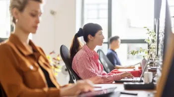 Funcion�rios em escrit�rio iluminado, com foco em uma mulher olhando para um monitor