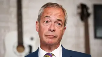 Nigel Farage em um close-up, vestindo terno azul, camisa branca e gravata listrada.