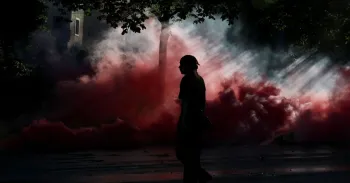 Pessoa caminha em meio a nuvens de fuma�a durante protesto em Genebra contra a pr�xima c�pula do G7 em 14 de junho de 2026 Denis Balibouse/Reuters