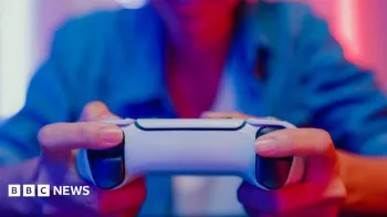 Close up das m�os de uma mulher segurando um controle de videogame, com ilumina��o colorida refletindo em um monitor � sua frente. Getty Images