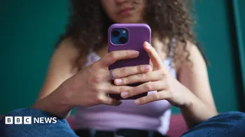 Uma jovem, cujo rosto n�o pode ser visto, senta-se de pernas cruzadas enquanto segura e usa seu smartphone. Ela usa jeans azul e um colete lil�s.